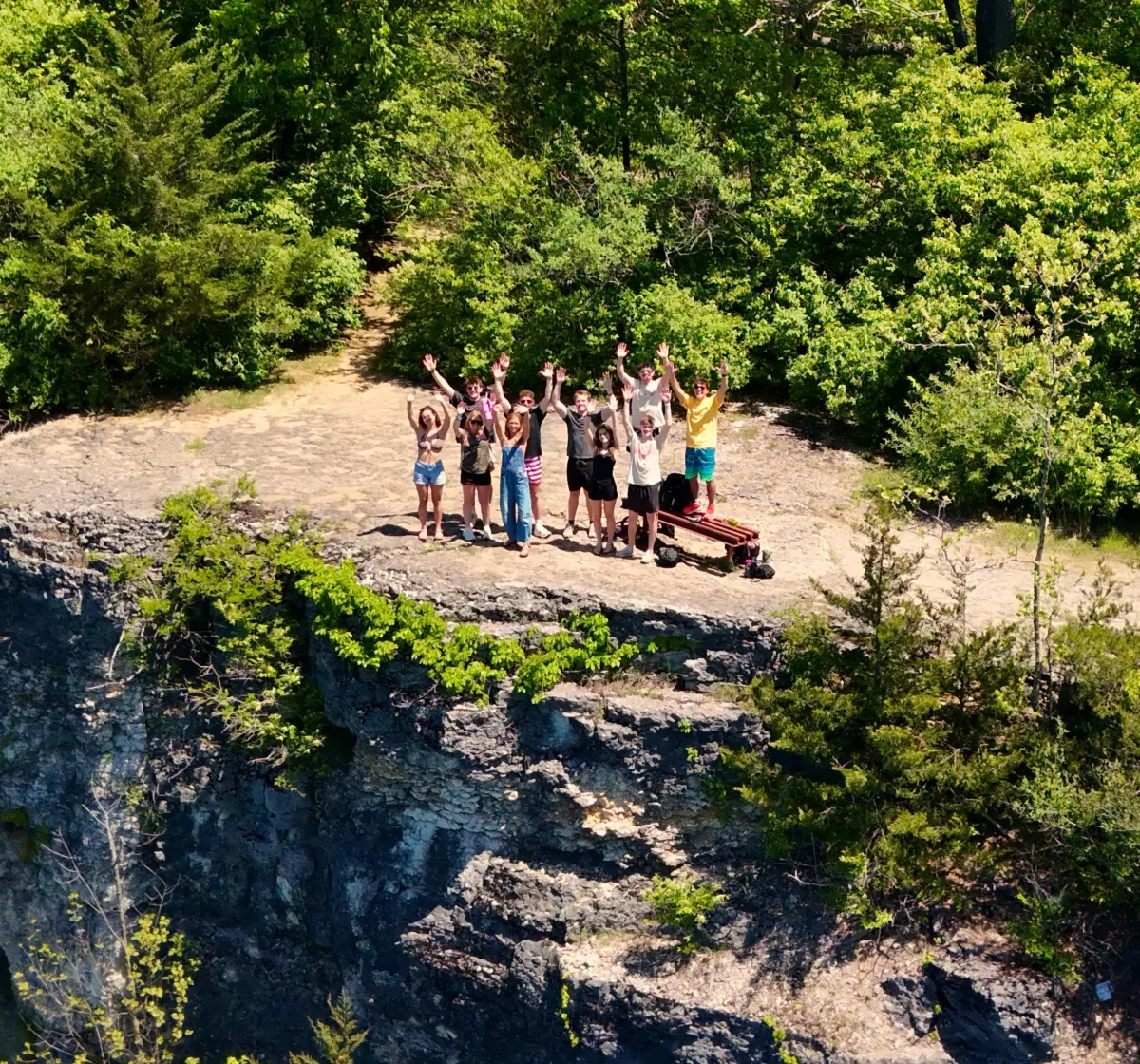 A happy group of people on the side of a cliff smile as the drone takes their photo